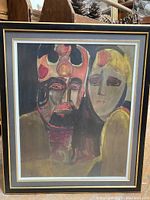 Framed abstract print showing two stylized faces of a couple in orange, black, and muted yellow tones with a black frame and white matting.