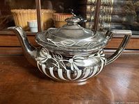 Side view of the vintage silver and white painted floral teapot showing spout, handle, and lid with leaf design.