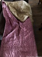 Full view of comforter draped over furniture showing pink front and gold reverse sides with quilted design.