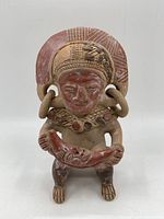 Front view of the ceramic figurine showing the full figure with large circular earrings and the canoe-like object held in hands