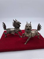 Pair of vintage Chinese metal Qilin figurines on red cloth background showing detailed side profiles.