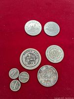 Photo of coins, including 1962 Canadian Silver Dollar, Mexican Peso, US nickels, and Wooden Nickel token on red background.