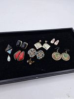 Full view of all twelve pairs of vintage earrings on a black surface, showing variety in styles and colors.