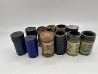 Frontal view of ten Edison player cylinders in their original cylindrical containers of various colors and label styles.