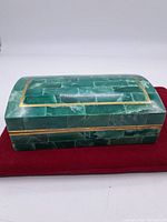 Closed view of the rectangular malachite box showing the green stone tiles with brass trim on a red cloth.