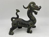Side view of the metal dragon figurine showing its entire body, curled tail, and horned head.