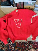 Full view of vintage red knitted sweater with large textured red 'V' outlined in white on front, ribbed cuffs and waistband.