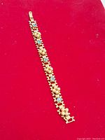 Full length image of the vintage gold-tone Coro bracelet laid flat on a red background showing the alternating blue stones and pearl clusters.