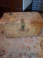 Front view of the vintage wooden box with visible metal latch on the lid and worn wood surface.