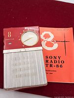 Front view of the vintage Sony TR-86 transistor radio next to the red instruction manual.