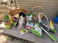 One photo showing three rattan baskets, plaster fairy statuette, packets of gardening soil and seeds, pruner, garden tools, and tea lights arranged on a bench.