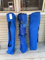 Three blue carrying bags containing folded portable camping chairs placed side by side on a wooden porch.