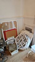 Wide view of all frames and cork boards stacked on floor in corner of room showing various sizes and styles including windowpane style frames and red cork boards.