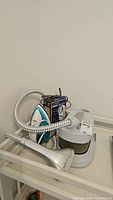 Photo showing Homestyles clothing steamer, Rival iron and box for Conair fabric defuzzer with hose coiled on steamer