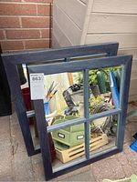 Two wooden window-frame style mirrors with divided panes, stacked leaning against wall outdoors, showing scratches and wear on the blue/dark wood frames.