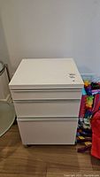 Full view of the white plastic coated side table with three drawers and wheels, showing its overall condition and design.