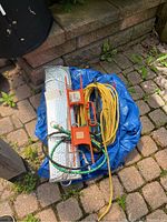 Items on ground including blue tarp, foil car sunshade, yellow extension cord, bungee cords and orange reel.