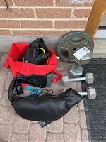 Displays two 25 lbs metal weight plates, two 10 lbs hex dumbbells, black resistance bands, a belt, and a black massage unit with accessories.