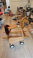 Side view of the wooden rocking horse alongside the ride-on toddler car. Rocking horse has a carved horse head and yarn mane. The toddler car is simple with four small wheels.