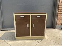 View of closed steel cabinet showing brown doors and drawers with silver handles, cream frame, and brown top.