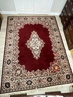Photo showing red area rug with cream floral medallion and patterned border, set in a room with wood and tile flooring.