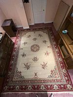Area rug viewed from above showing floral central medallion and scattered floral patterns, bordered in red with floral and geometric details.