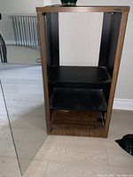 Front view of the audio cabinet with the glass door open, showing the wood and black shelving inside.