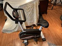 Full side and front view of the exercise bike showing adjustable padded seat, pedals, and handlebars.