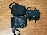 Three laptop bags laid on the floor: Dell black canvas, Danier black leather, and Air Canada green canvas.