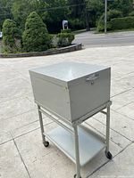 Metallic filing cabinet on wheeled stand.