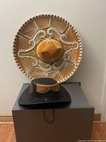 Front view of Mexican sombrero hanging on wall and black leather Panama style cowboy hat placed on a box beneath it.