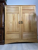 Front view of oak finish tan colored clothing cabinet with two doors and brass pull handles