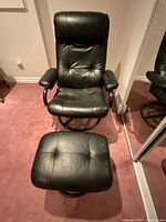 Front view of black leather recliner chair with padded seat and backrest along with matching ottoman.