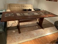 Long view of the solid rosewood table extended with two slabs. Shows the trestle base and stone inlay in the center.