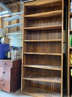 Front view of the tall, solid wood bookcase showing six shelves with dark oak finish and wood grain texture.