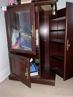 Front and angled view showing glass door open with items inside, two wooden doors open showing compartments and open shelving on side for CDs and DVDs.