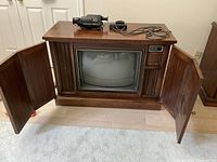 Wide shot of Zenith wooden cabinet TV with two side doors open revealing the screen and speaker areas, with vintage black handheld video camera and remote control phone on top.