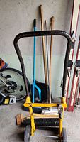 Front view of the yellow and black dolly with multiple brooms behind it