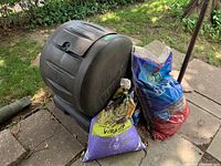 Overview of black rotating composter drum with three garden supply bags at side