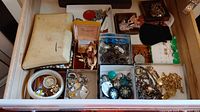 Overhead view of nine small trays and a snakeskin pouch filled with assorted jewelry pieces