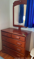 Front view of wood dresser with attached mirror reflecting window and curtains, showing five drawers with wooden handles and surface scratches.