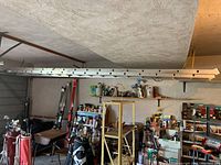 Aluminum extension ladder hanging horizontally in a garage setting with other tools and equipment.