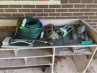 Garden hose coiled with four sprinklers spread out on a shelf next to a brick wall.