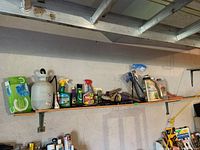 Shelf with assorted gardening supplies including sprayer, hanging brackets, shears, and bottles