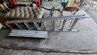 Side view of an aluminum ladder on a concrete floor beside a sofa and round table, showing ladder length and condition.