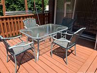 Full view of the patio dining set on a wood deck including table with glass top and four matching chairs.