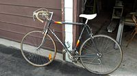 Full side angle view showing black Peugeot road bike with drop handlebars, white saddle, and 26" thin tires.