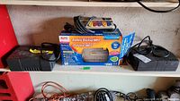 Two APC battery backup units and a power bar on a shelf, including a boxed Back-UPS ES 500 model and a smaller unboxed unit.