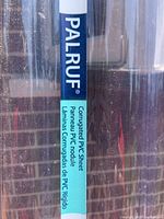 Close-up photo showing the Palruf brand label on a clear corrugated PVC sheet specifying it is a corrugated rigid PVC sheet.