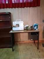 Wide view showing entire sewing table with sewing machine and supplies placed on top against wood panel wall.